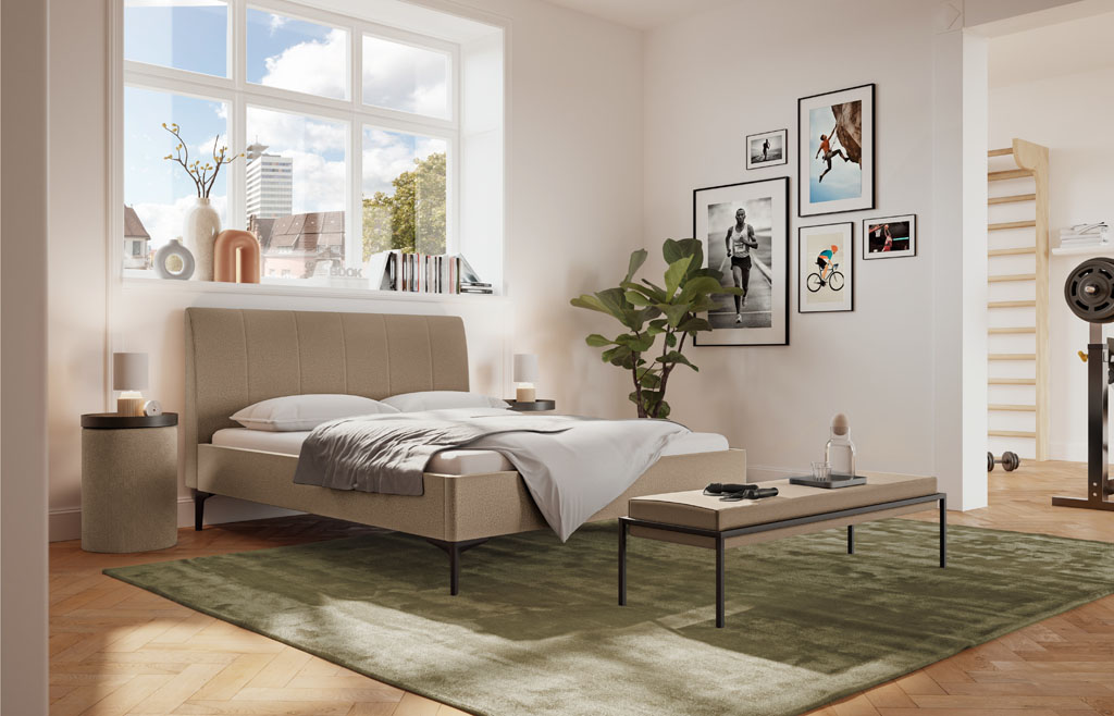 Sandfarbenes Polsterbett mit vertikal gestepptem Kopfteil und schwarzen Füßen in einem warmen Schlafzimmer mit grünem Teppich und großen Fenstern (KI-generiert)