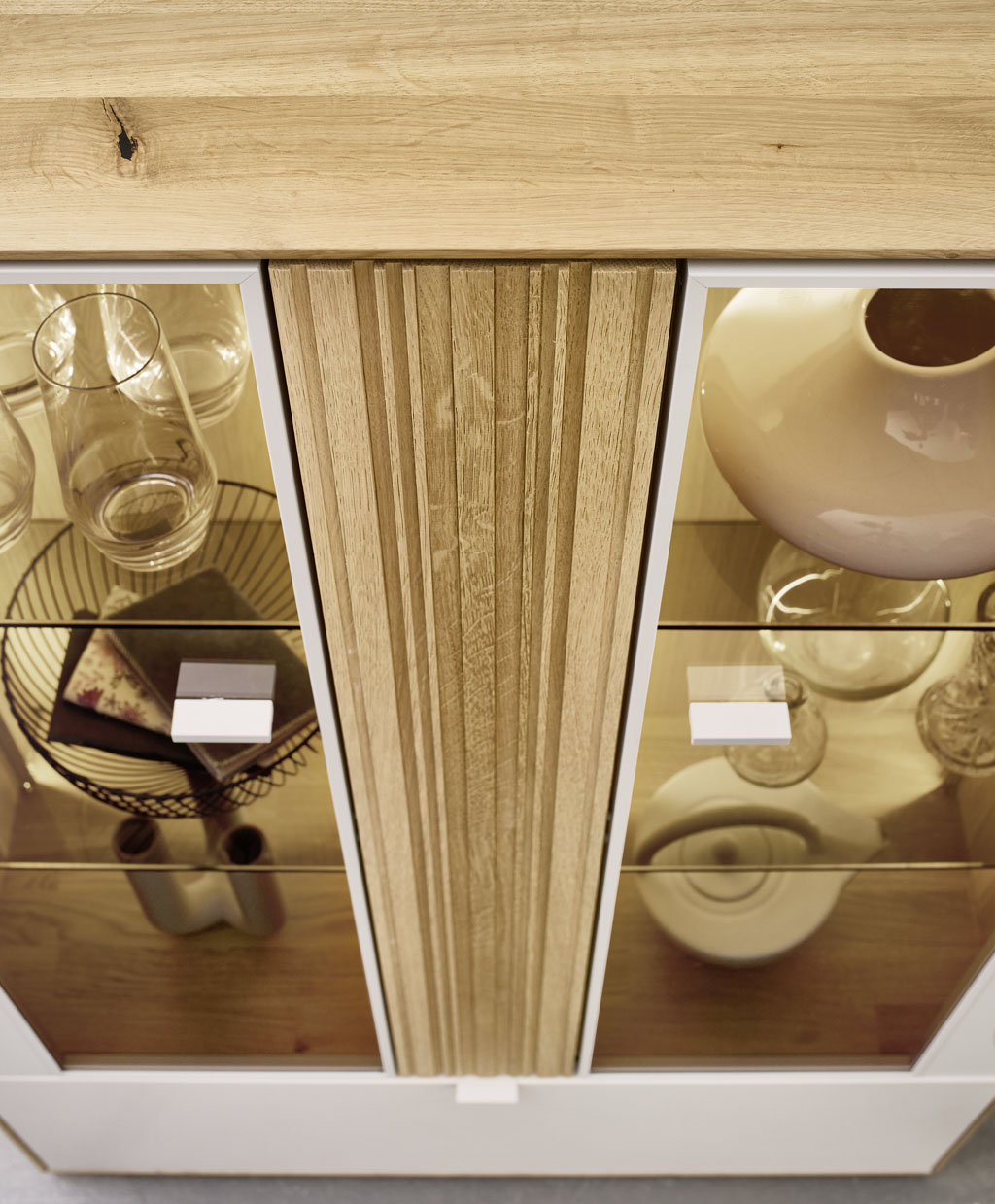 Detailaufnahme von oben eine Vitrinenschrankes mit markantem Holzakzent weiß-braun mit Glasvitrinenfächer