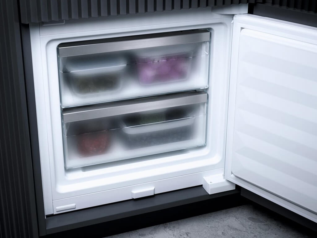 Das Bild zeigt die zwei Gefrierschubladen eines Miele-Kühlschranks, die von oben zu sehen sind. Die Schubladen sind transparent und haben Edelstahlgriffe, in denen sich bereits gefrorene Lebensmittel in rechteckigen Behältern befinden.