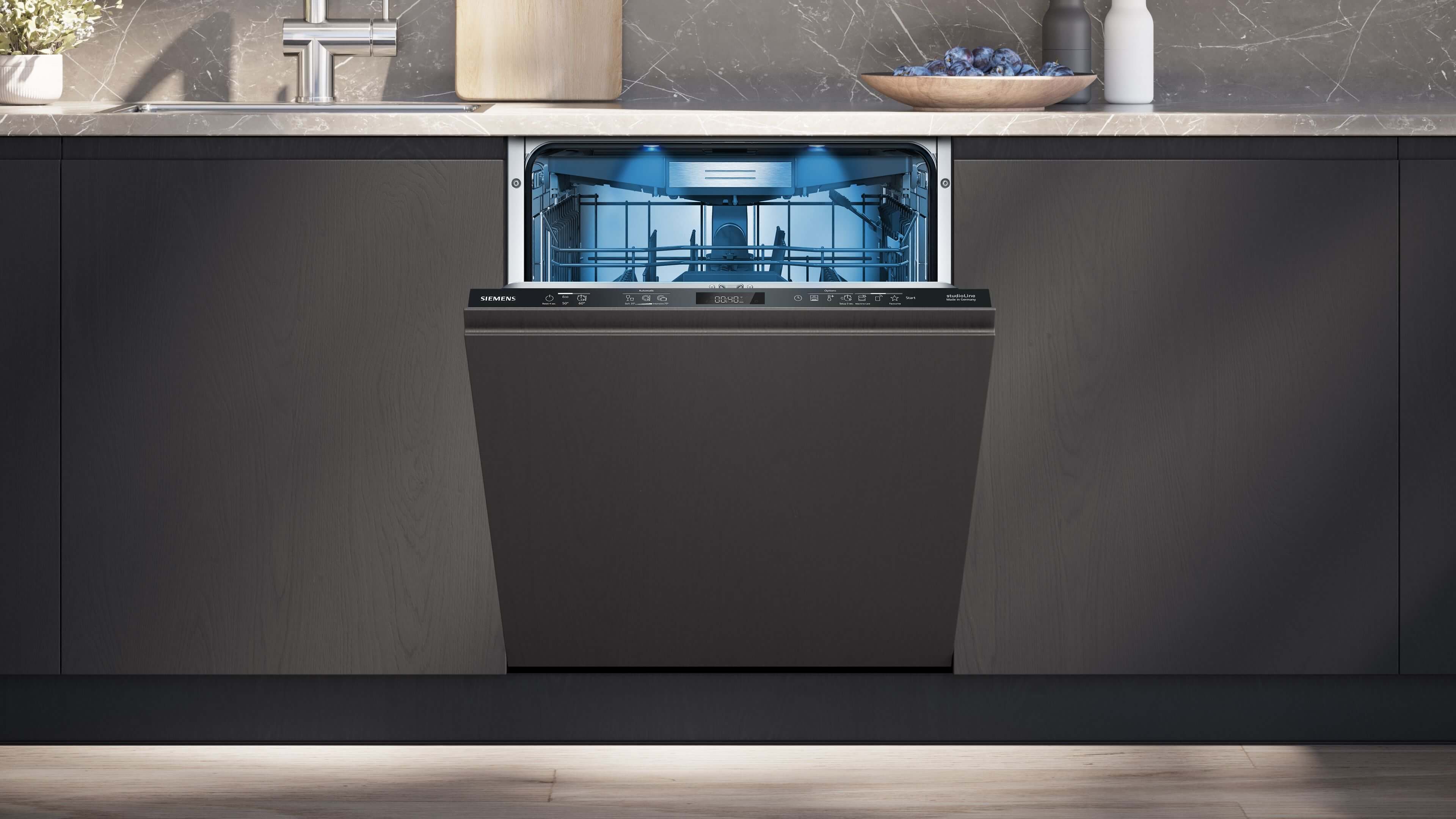 Ein in eine dunkle Küchenzeile eingebauter Siemens-Geschirrspüler mit dunkler Möbelfront, bei dem die Bedienblende sichtbar ist und der Innenraum blau beleuchtet leuchtet.