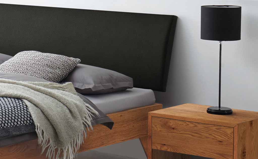 Schlafzimmer mit einem Bett, grauen Kissen, einer Decke, einem Holz-Nachttisch und einer schlanken schwarzen Lampe