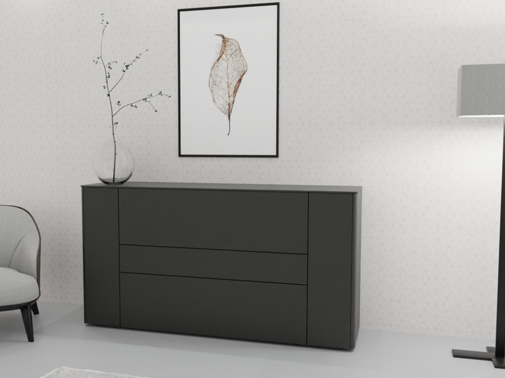 Sudbrock Goya - Sideboard | 2 Türen, 2 Schubladen, 1 Klappe | B: 175,2 cm | Lack quarz Schwarz lackierter Sideboard-Schrank neben einem Sessel mit einem dekorativen Zweig in einer Vase und einem gerahmten Blattdruck an der Wand.