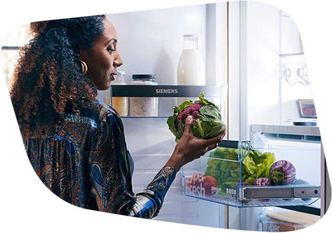 Frau steht vor geöffneter Kühlschranktüre und schaut sich ihr Gemüse genauer an. Sie ist von der Frische der Lebensmittel dank ihrem Siemens Kühlschrank begeistert!