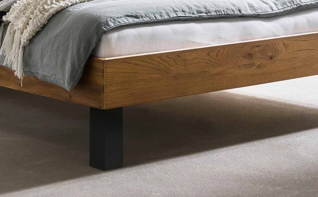 Detailansicht eines modernen Holzbetts mit grauer Bettdecke und schwarzen Beinen.