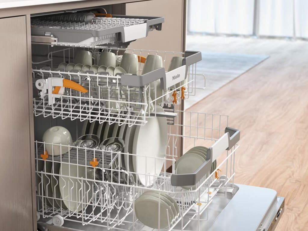 Innenansicht eines geöffneten Miele Geschirrspülers, beladen mit Tellern, Tassen, Gläsern und Besteck in den oberen und unteren Körben.