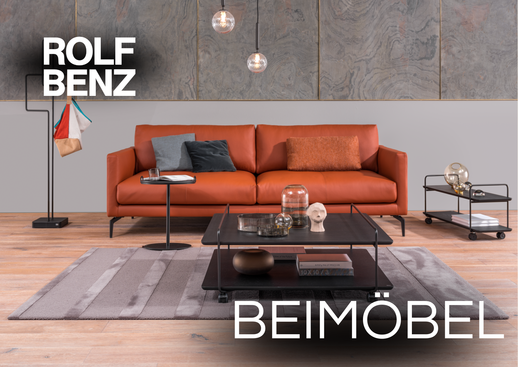 Wohnzimmer mit roter Couch und Beimöbel. Aufschrift: Rolf Benz Beimöbel.