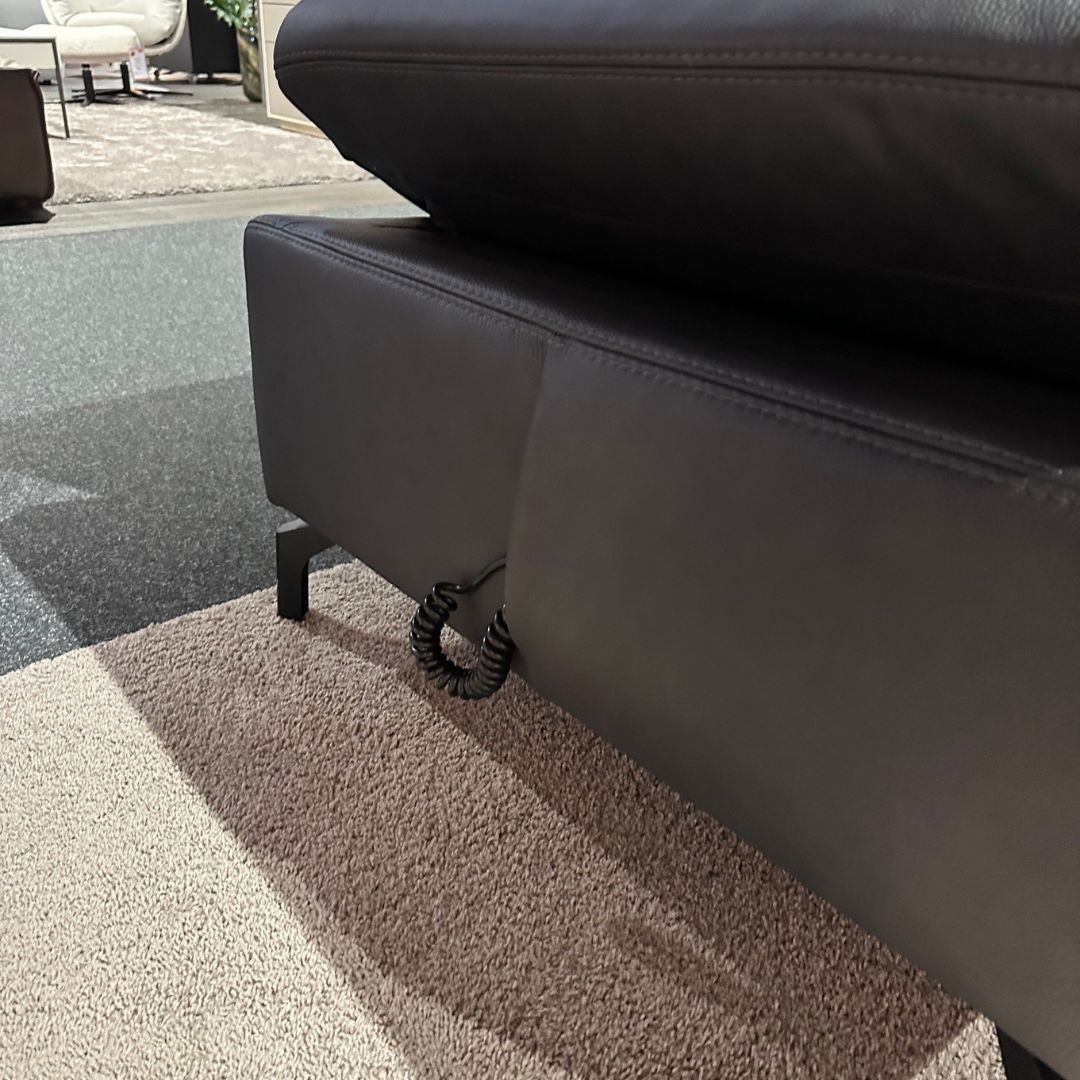 Nahaufnahme eines schwarzen Ledersofas mit verstellbarer Rückenlehne und Polsterung auf einem Teppichboden