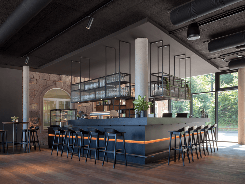 Elegante, moderne Bar mit hohen Hockern und Hängeregalen in hellem, offenem Raum