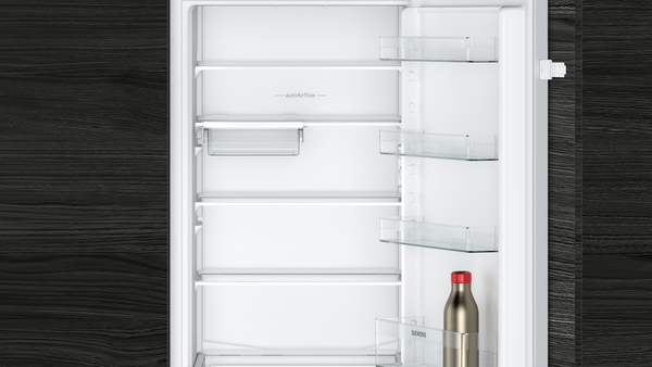 Ein geöffneter Einbaukühlschrank mit leerem Innenraum, darin eine Edelstahlflasche in der Türablage.