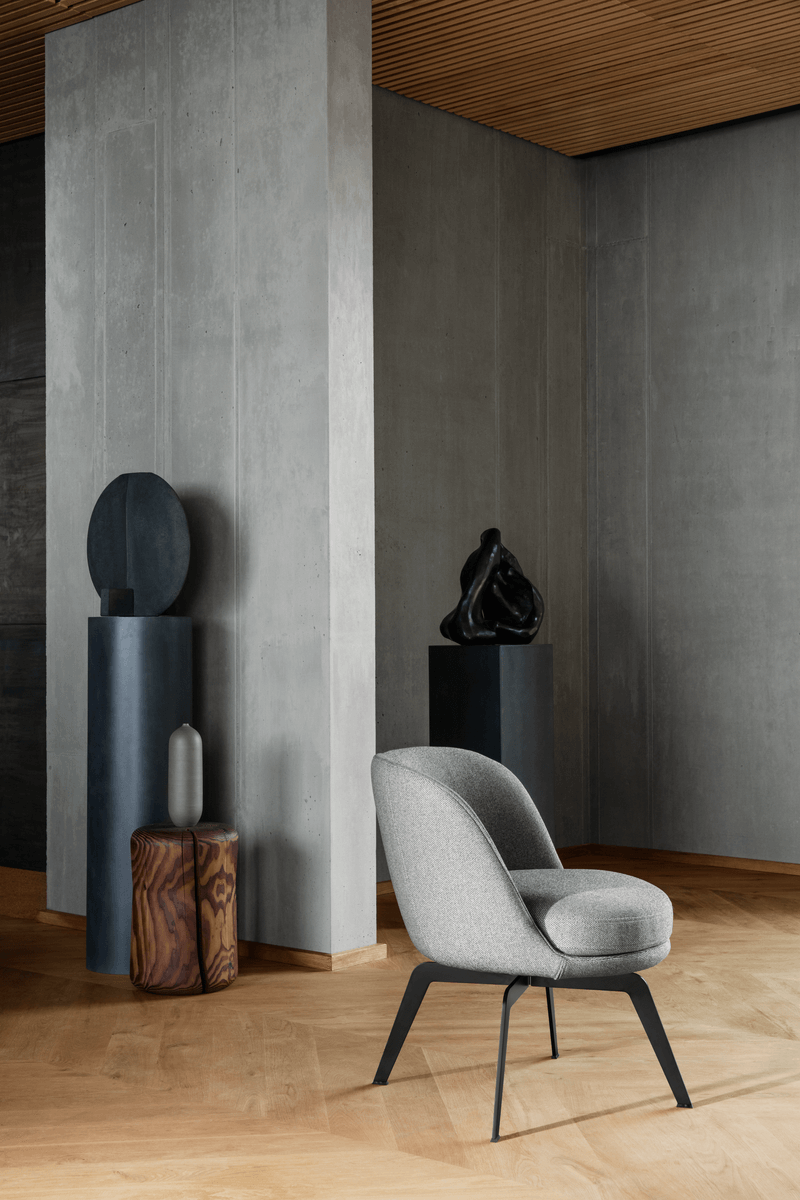Ein stilvoller grauer Stuhl vor einer Betonwand, umgeben von modernen Skulpturen auf Sockeln in einem elegant gestalteten Raum.
