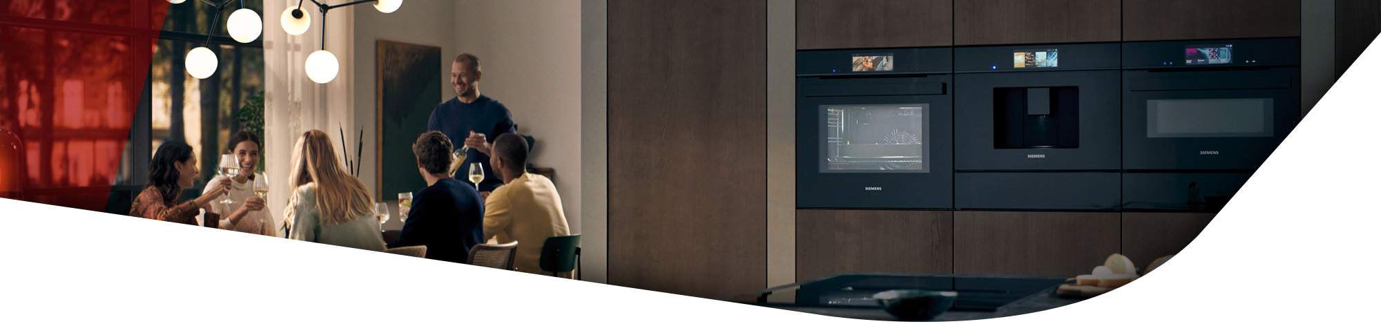 Designer Elektrogeräte (Backofen, Dampfbackofen und Kaffeemaschine) in einer offenen Küche. Im Hintergrund sind Menschen zu sehen, die abends bei einem gemütlichen Abend zusammensitzen.