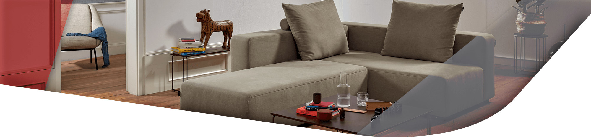 Ein modernes Wohnzimmer mit einem beigen modularen Sofa, dekoriert mit Büchern und einer Holzfigur auf einem Beistelltisch.