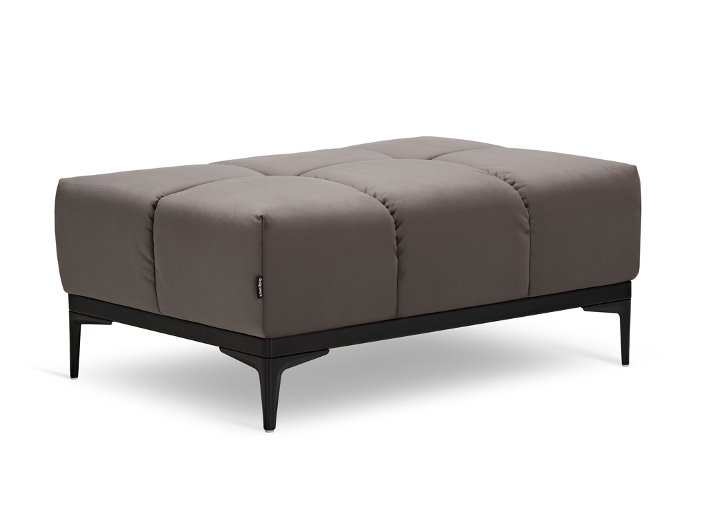 designwerk Oasis - Megahocker Ein gesteppter Hocker mit braunem Stoffbezug welcher auf einem schwarzen Gestell mit spitzen Füßen steht.