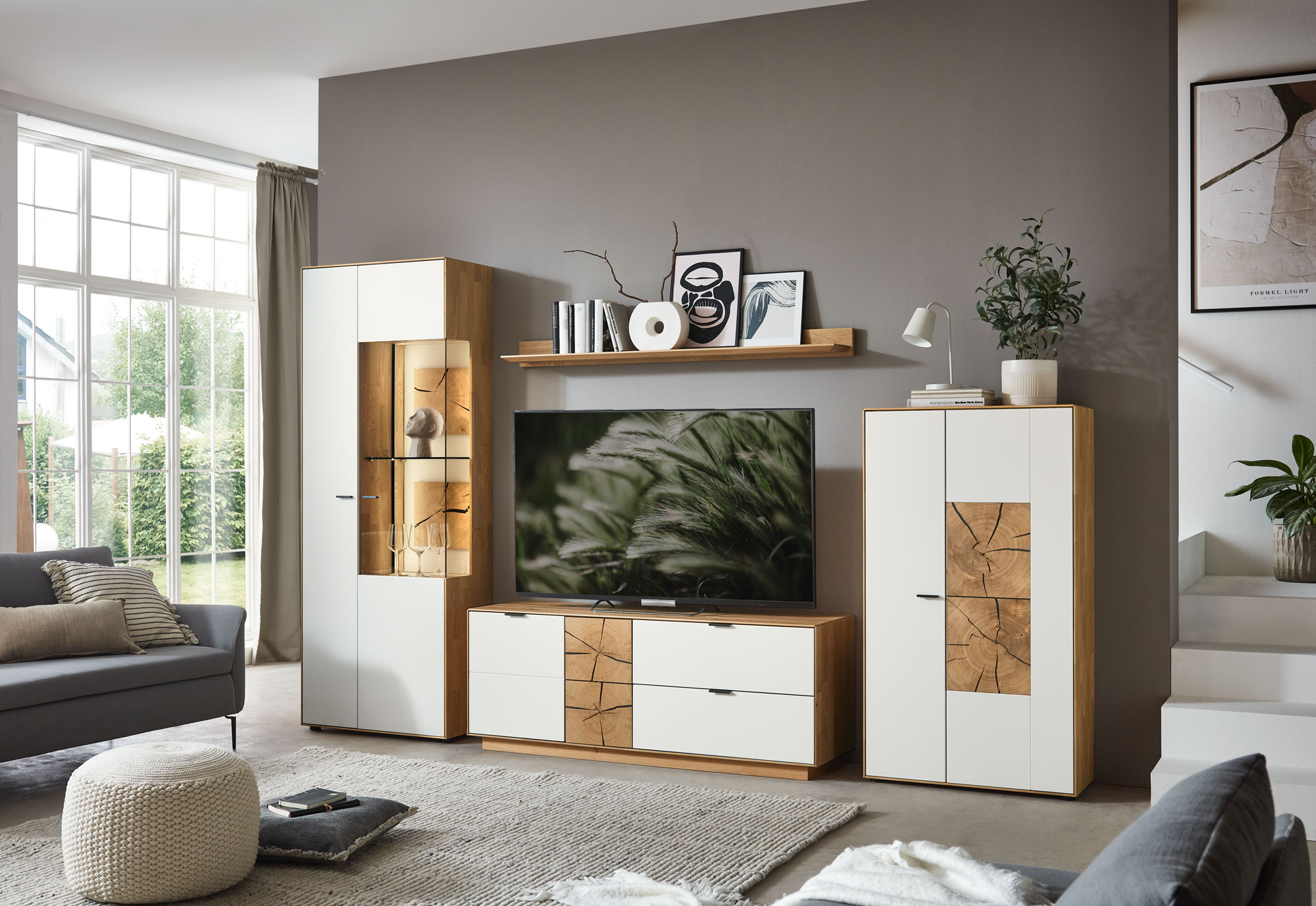 Wöstmann WM 2410 - Wohnwand | Type 0015/0115 | Lack und Wildeiche massiv | Hirnholzakzent Wohnzimmer mit großem Fenster, grauem Sofa, dekorativem TV-Möbelset in Holz- und Weißtönen, Pflanzen und modernem Design