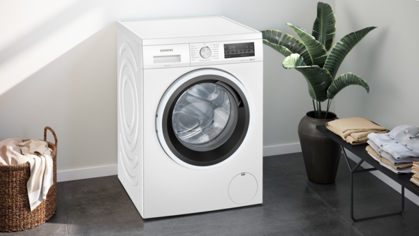 Weiße Waschmaschine in einem modern eingerichteten Badezimmer mit Pflanzen und Wäschekorb