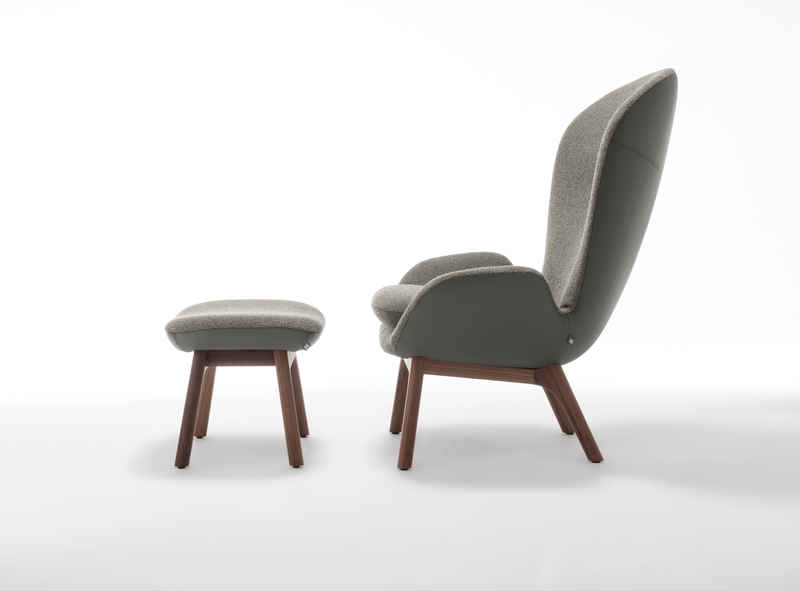 Grauer Sessel mit hoher Rückenlehne und passendem Hocker, beide mit Holzbeinen, seitliche Ansicht