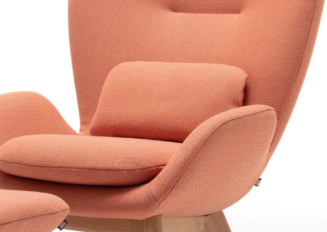 Detailaufnahme eines pastellrosafarbenen Polstersessel mit markanten Armlehnen und Rückenkissen vor weißem Hintergrund