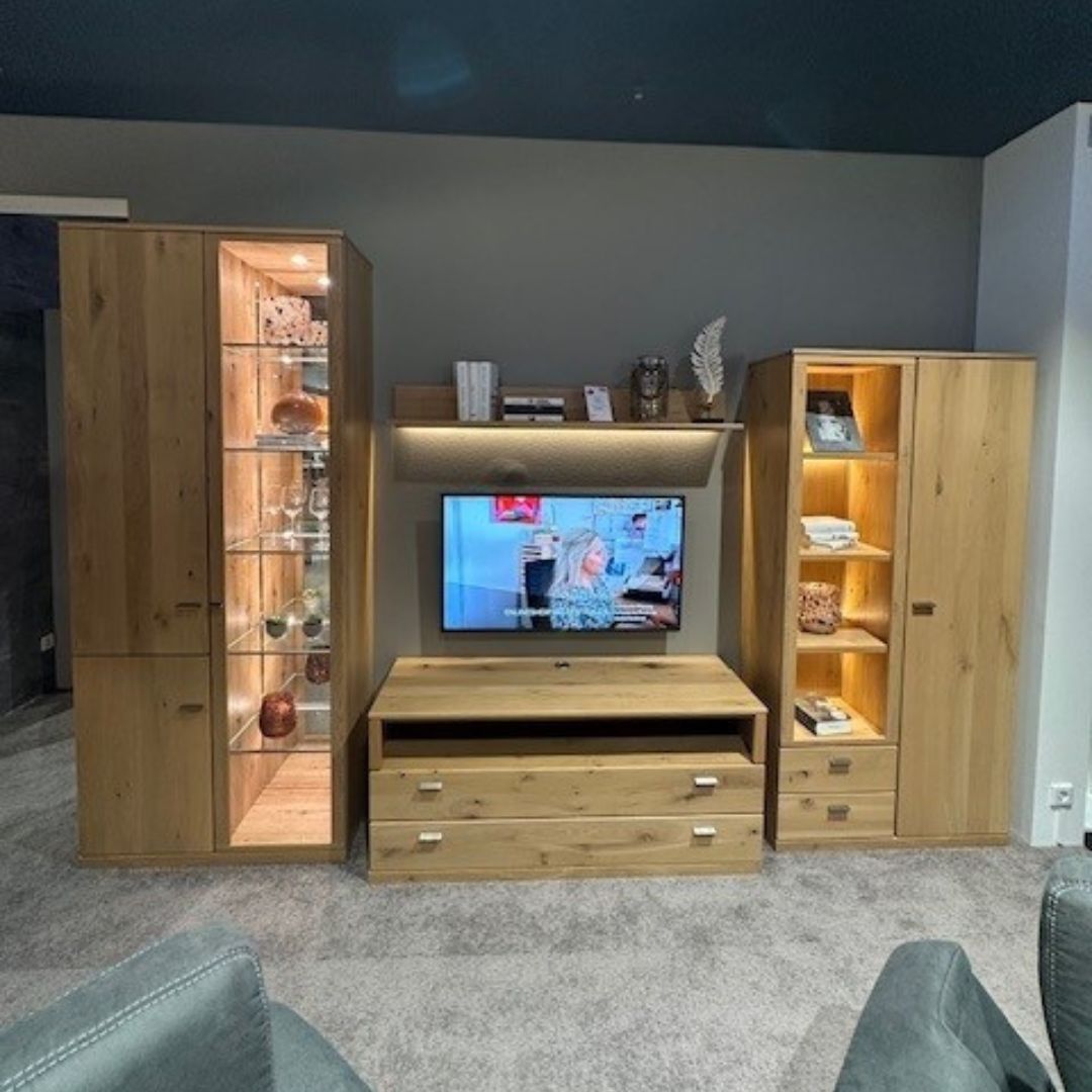 RMW ALLEGRO | Wohnwand Wohnzimmerschrank aus hellem Holz mit Glastür und Regalen, Fernsehbildschirm und dekorativen Elementen, beleuchtet im modernen Wohnzimmer