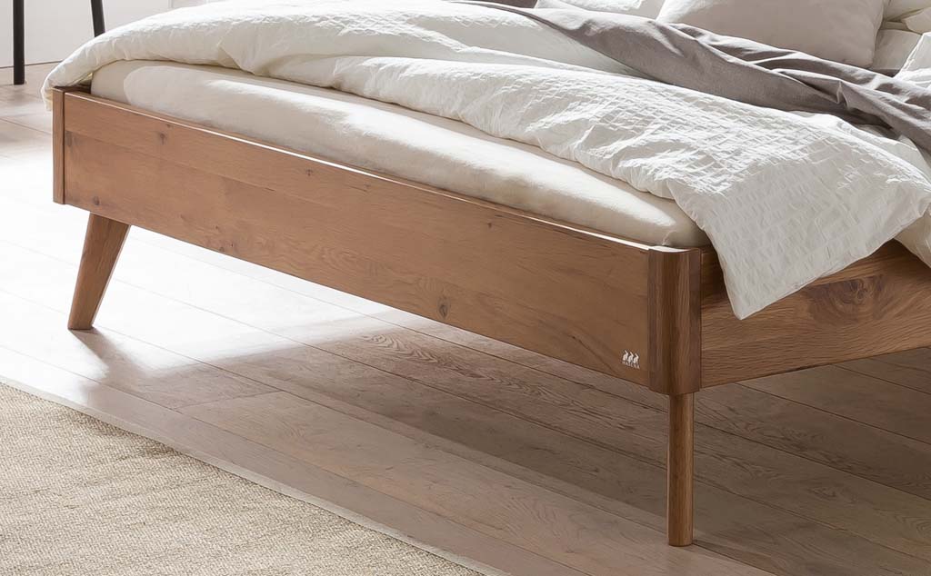 Detailaufnahme eines braunen Holzbettes mit Holzfüßen in einem hellen Raum