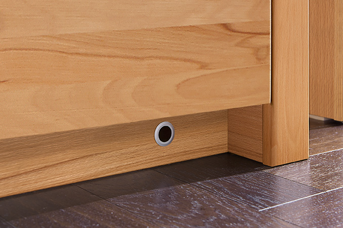 Nahaufnahme eines Holzmöbels mit einem kleinen runden Belüftungselement auf einem dunklen Holzboden