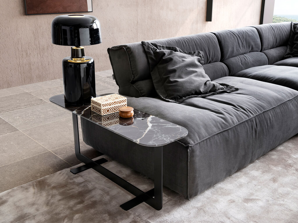designwerk Tische - Couchtisch One Blade long | 110 x 32 cm Ein graues Sofa mit einem modernen Beistelltisch aus Marmor, darauf eine schwarze Tischlampe und zwei dekorative Boxen.