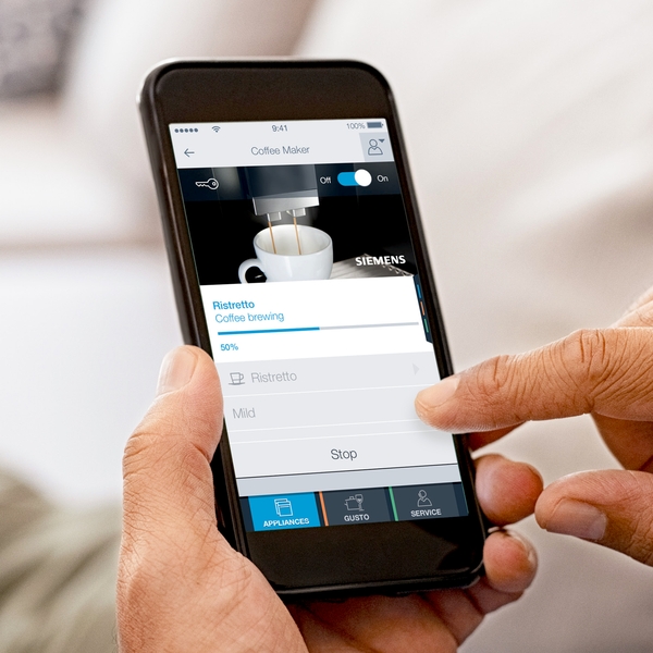 Person verwendet App auf einem Smartphone zur Steuerung einer Kaffeemaschine