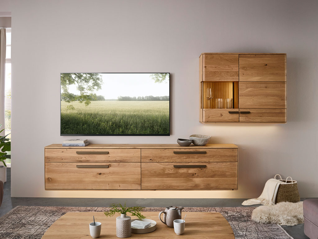 moderne Wohnwand aus Holzt mit großem Hängelowboard und einem Hängeschrank mit Vitrinenausschnitt und Beleuchtung stilvoll dekoriert in einem modernen Zimmer