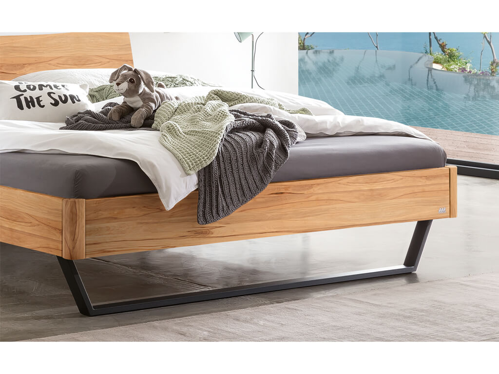 Nahaufnahme der Füße und des Bettrahmens vom Hasena Bett Tresali aus Wildbuche, das vor einem Fenster mit Pool-Blick steht.