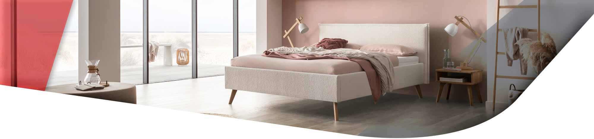 Im Mittelpunkt steht ein beiges Doppelbett mit einem weichen, strukturierten Kopfteil. Es ist mit rosafarbenen und grauen Decken und Kissen dekoriert.