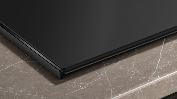 Detailansicht der Ecke des Siemens Induktionskochfelds. Gezeigt wird die extrem matte, reflexionsarme Oberfläche und die präzise Verarbeitung der Glaskante auf einer Marmor-Arbeitsplatte.