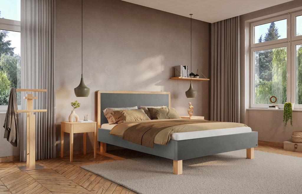 Graues Polsterbett mit hell geölten Eichenfüßen und gerahmtem Kopfteil in einem hellen, gemütlichen Schlafzimmer mit Holzfischgrätboden und großen Fenstern (KI-generiert)