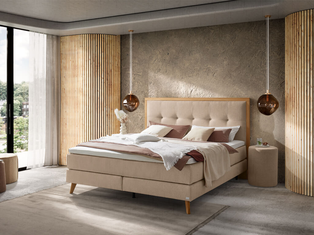 Ein helles Schlafzimmer mit einem beigefarbenen Boxspringbett mit einem gepolsterten Kopfteil und passenden Nachttischen.