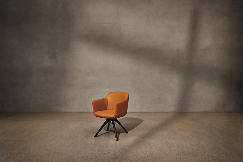 Ein eleganter, orangefarbener Stuhl mit schwarzem Drehgestell steht vor einer grauen Wand in einem minimalistischen Raum.