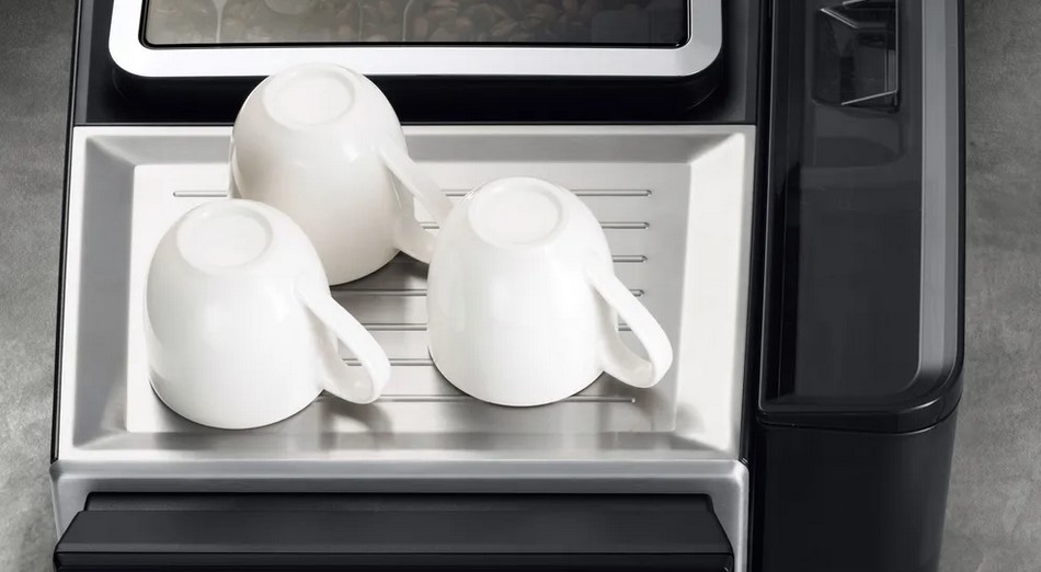 Drei weiße Tassen umgedreht auf einem Tassenwärmer einer schwarzen Kaffeemaschine