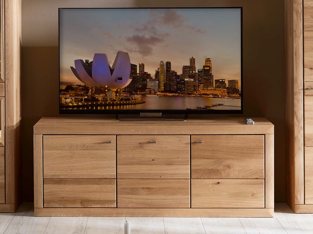 Ein moderner Fernseher auf einem Holzschrank mit einer abendlichen Stadtlandschaft auf dem Bildschirm.