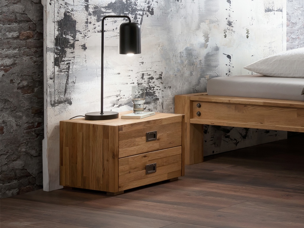 brauner Holznachttisch mit zwei Schubladen und markanten eingelassenen Metallgriffen stehend neber einem Bett stilvoll dekoriert Lica von Hasena