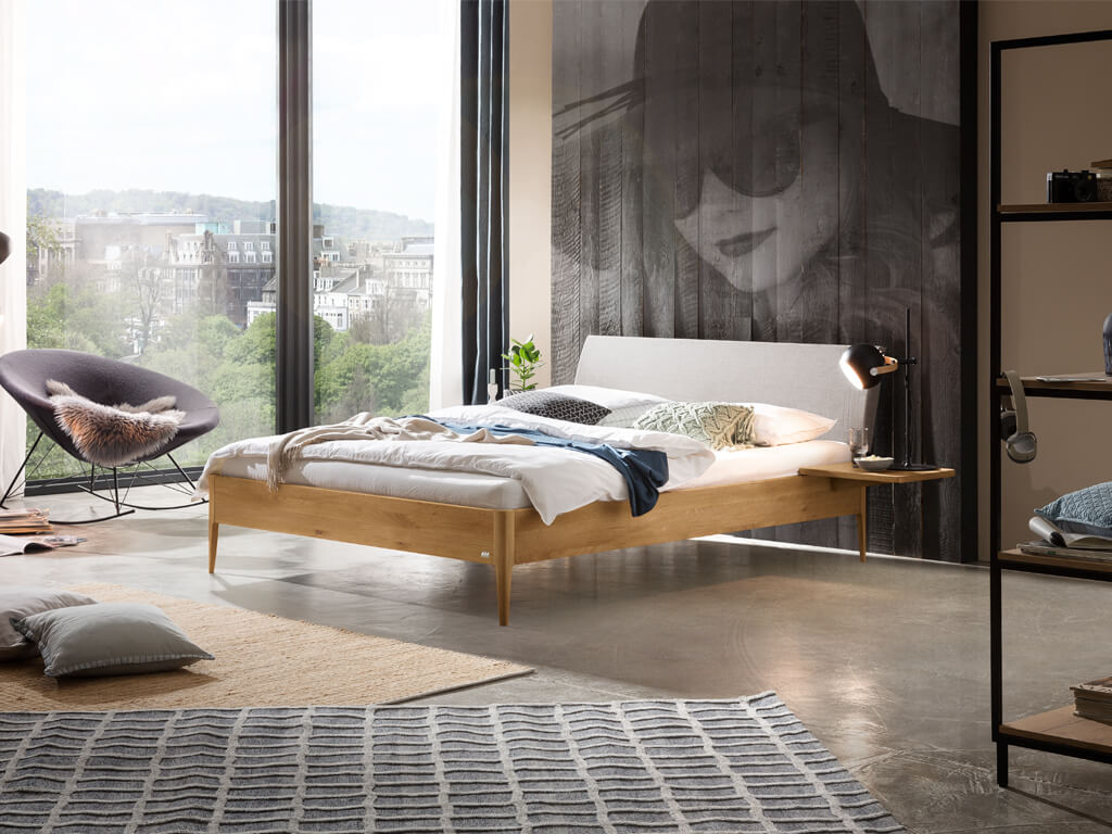 Hasena -  Lounge Bett Fanano | Polsterkopfteil Lecco | Holzfuß Pile | versch. Größen & Farben konfigurierbar Holzbett mit hellgrauem Polsterkopfteil und Holzablage direkt am Bettrahmen zur Ablage als Nachttisch