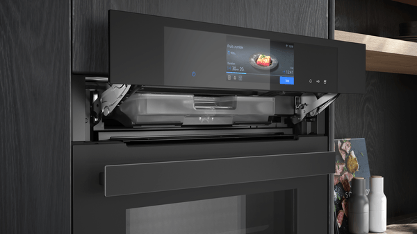 Nahaufnahme der hochgefahrenen Bedienblende des Siemens iQ700 Dampfbackofens. Dahinter wird der entnehmbare Wassertank sichtbar.