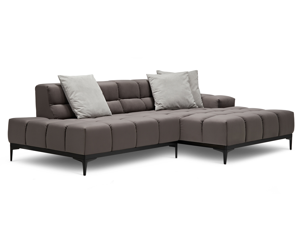 Ein L-förmiges, modulares Ecksofa in Dunkelgrau mit gesteppten Sitz- und Rückenkissen und schlanken schwarzen Metallfüßen. Zwei helle, graue Zierkissen liegen auf der Rückenlehne. Der Hintergrund ist weiß.