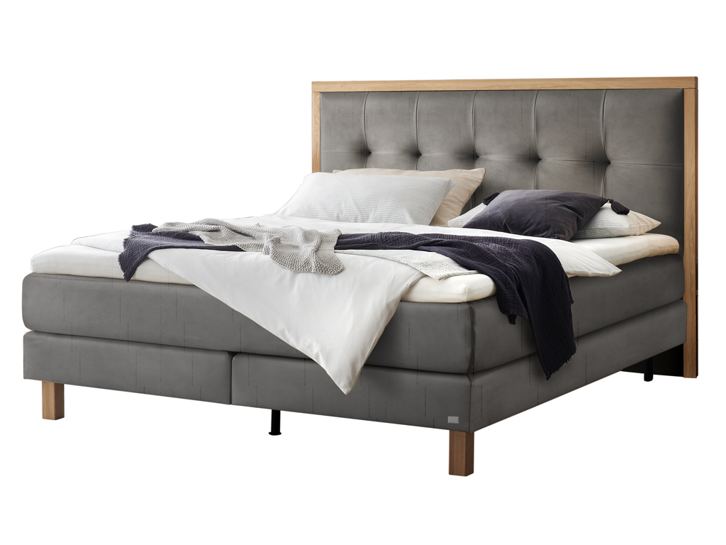 Ein freigestelltes Produktfoto des Boxspringbettes Hasena Pronto Solara mit stahlgrauem Stoffbezug und Holzrahmen, dekoriert mit Decken und Kissen.