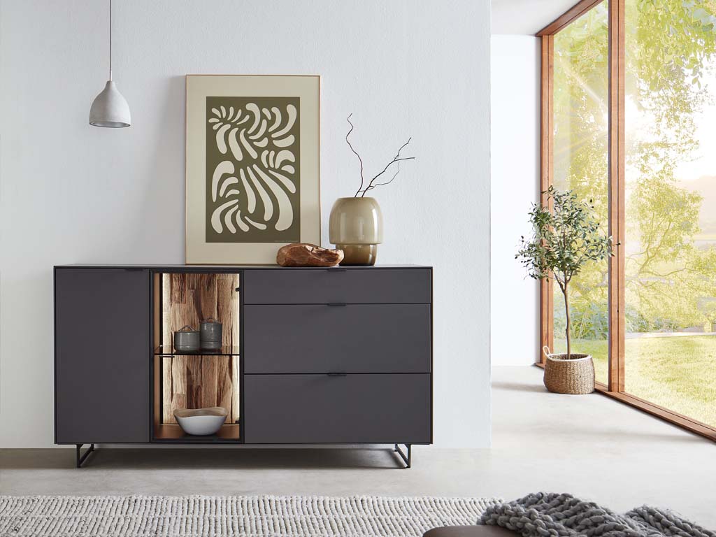 Wöstmann WM 2470 - Sideboard | Type 2543/2544 | B: 181,9 cm Ein modernes Sideboard mit künstlerischer Dekoration und Pflanzen in einem hellen Raum mit großen Fenstern.