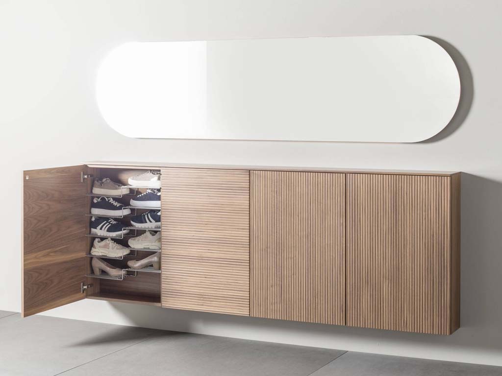 Schuhschrank aus Holz mit geöffnetem Fach, gefüllt mit Turnschuhen, und einem Spiegel darüber an der Wand