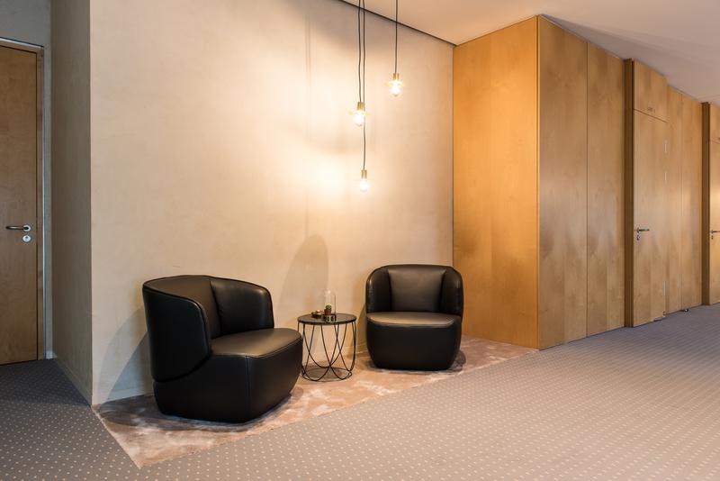 Gemütlicher Lounge-Bereich mit zwei schwarzen Sesseln und einem kleinen Tisch, dekoriert mit hängenden Glühbirnen.