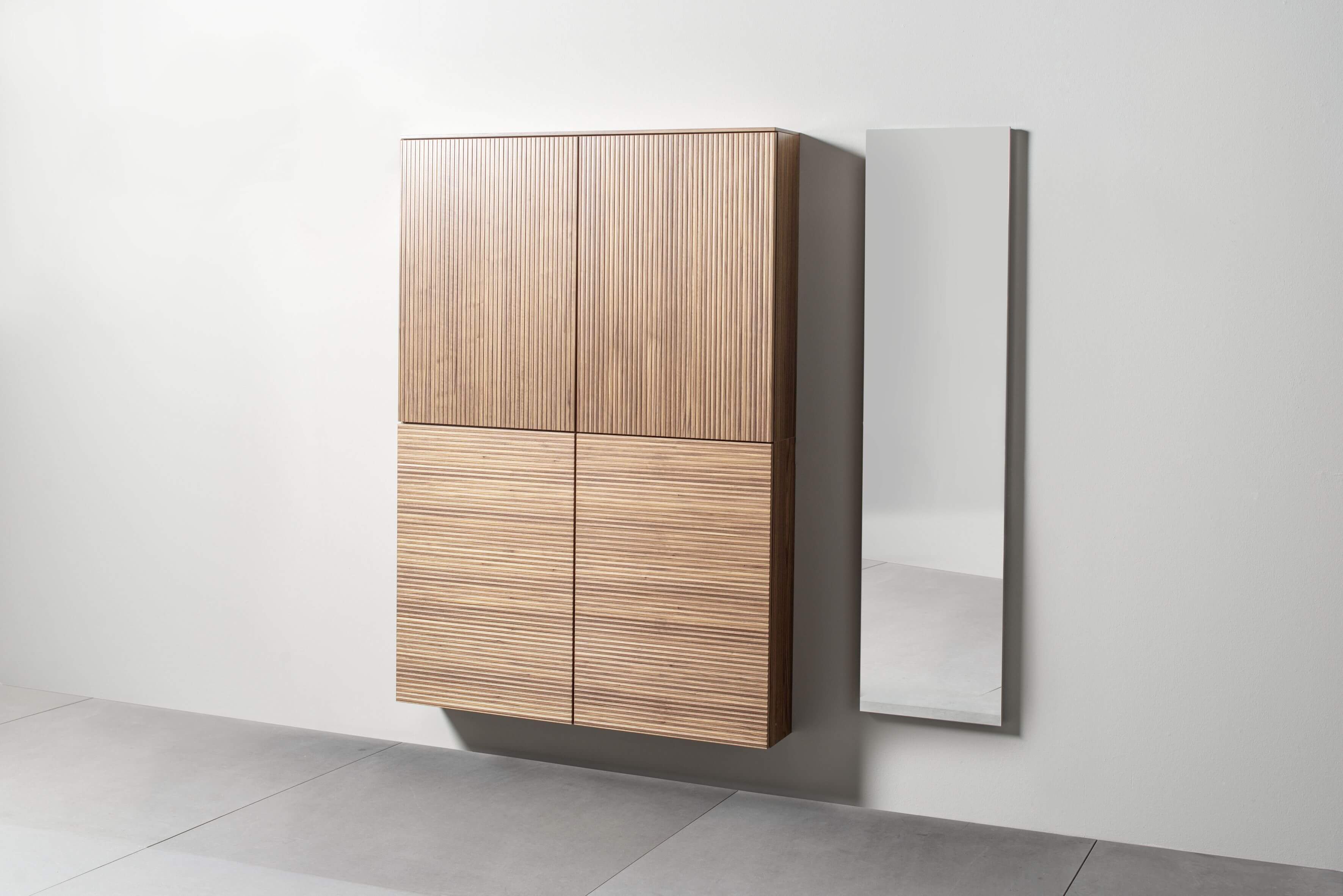 Sudbrock Tando - Schuhschrank (Rillenfront) inkl. Spiegel | Furnier Nussbaum natur  | B: 190 cm Ein moderner Wandspiegel neben einem hölzernen Wandschrank mit vertikalen Linien auf den Türen.