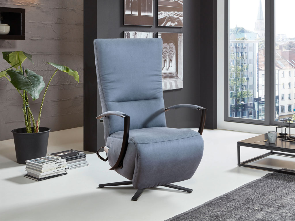Poco Dayton Style modern - Relaxsessel Ein eleganter grauer Relaxsessel mit hoher Rückenlehne steht in einem modernen Wohnzimmer mit großen Fenstern und urbaner Aussicht.
