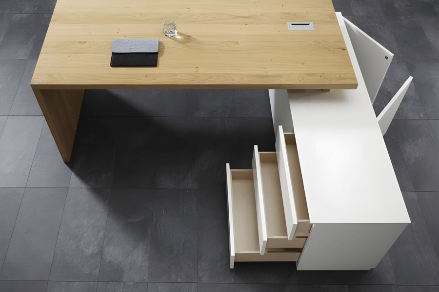 Schreibtisch von oben fotografiert. Man sieht einen geöffneten Rollcontainer