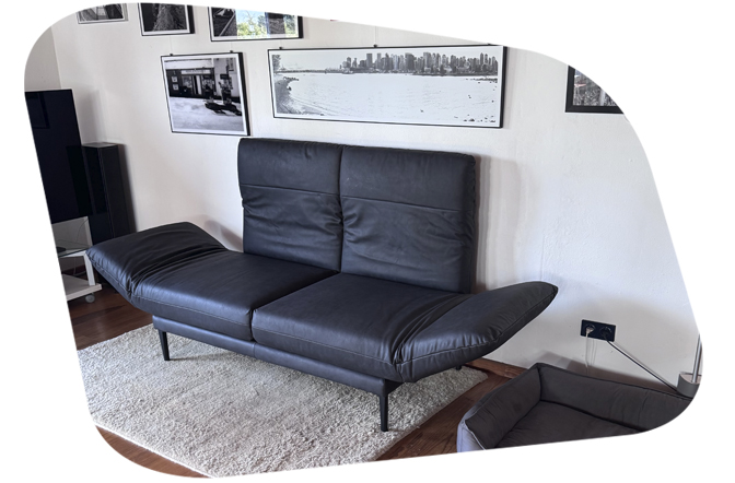 freistil 140 Sofabank in schwarzem Leder vor einer Bilderwand.