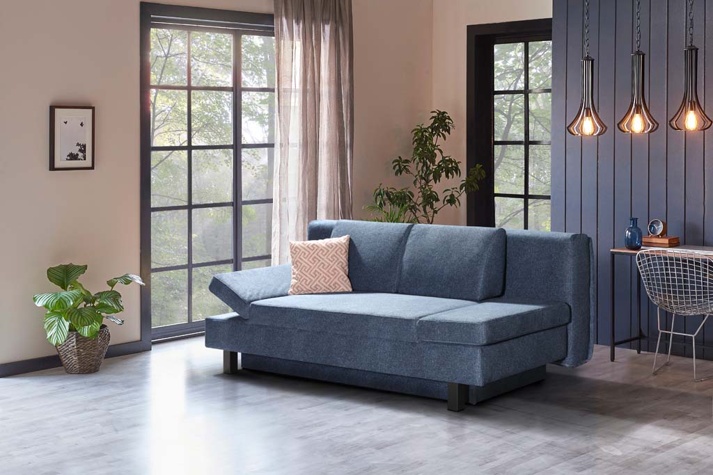 Restyl Tino - Schlafsofa (Querschläfer) | blau | mit Bettkasten | 150 x 200 cm Blaues Sofa in einem modernen Wohnzimmer mit großen Fenstern, Zimmerpflanzen und hängenden Lampen