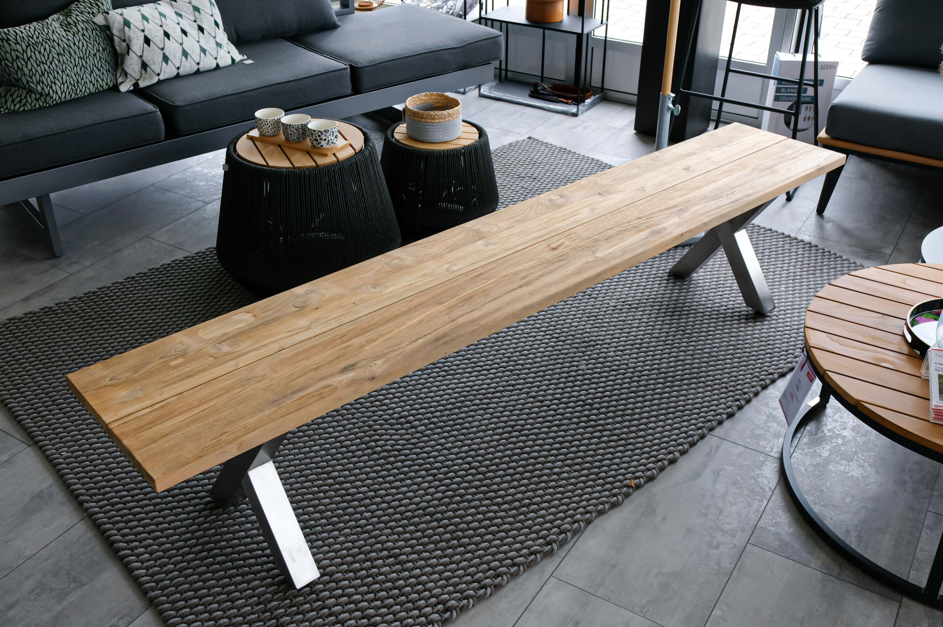 Eleganter Holztisch mit Metallbeinen in modernem Wohnbereich, umgeben von Sofas und runden Beistelltischen auf grauem Teppich