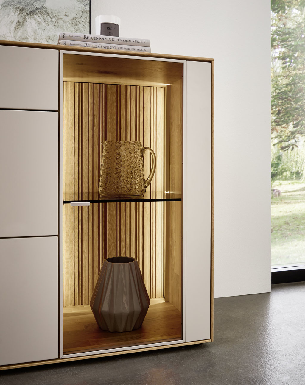 Detailaufnahme eines weiß-braunen Sideboards mit beleuchtetem Glasvitrinenschrank stilvoll dekoriert